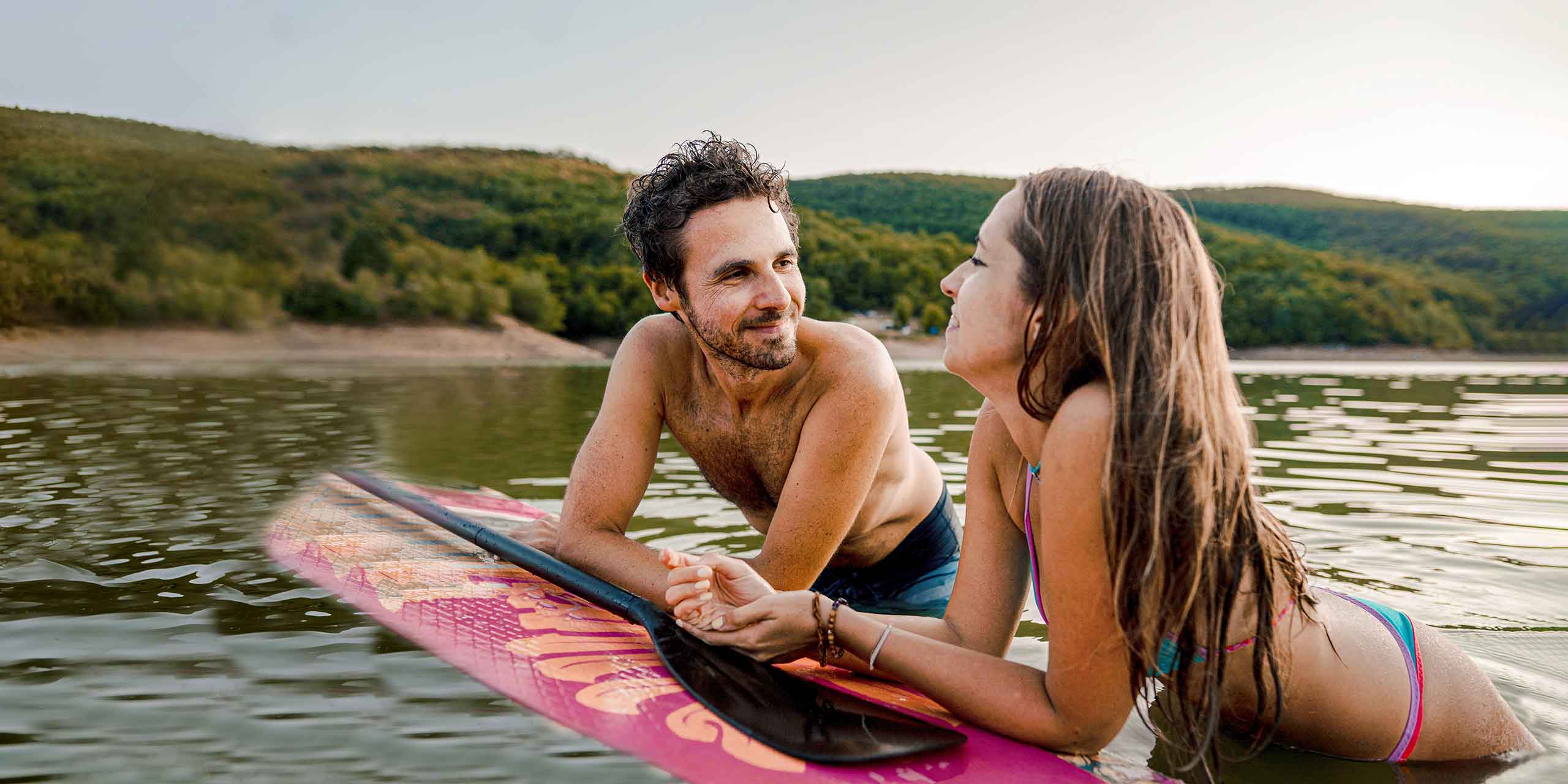 Zwei junge Menschen unterhalten sich auf einem Stand up Paddle im Wasser